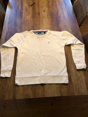 Vit sweatshirt från Gant - Klassisk vit sweatshirt från Gant med rund halsringning och diskret logga broderad på bröstet. Tröjan har ribbade muddar vid ärmslut och nederkant samt en mjuk insida. Perfekt för en clean och avslappnad stil.