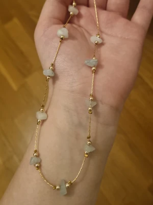 Guldfärgat halsband med ljusblåa stenar - Snyggt halsband med tunn guldfärgad kedja och oregelbundna ljusblåa stenar. Kedjan har små guldfärgade detaljer mellan stenar som ger ett unikt och trendigt intryck. Perfekt accessoar för att lyfta din outfit.