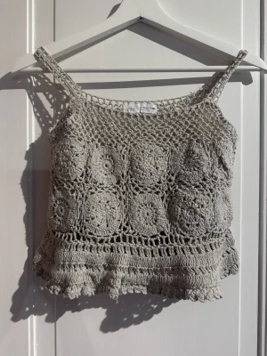     Virkad Zara topp med silverskimmer – 152 cm / 11–12 år - Beige virkad topp från Zara Kids i storlek 11–12 år / 152 cm. Fint crochetmönster med lätt silverskimmer i tyget, smala axelband och dekorativ kant nedtill. Fodrad framtill över bysten och annars lätt transparent.