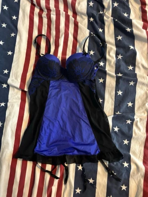 Blå och svart bustier med spets - Snygg bustier i blått och svart med spetsdetaljer över kuporna och tunna axelband. Framsidan har en slät blå panel och sidorna är i svart mesh. 