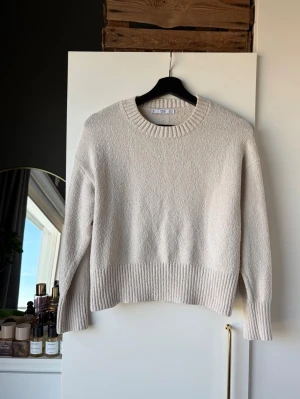 Beige stickad tröja - Snygg beige stickad tröja med rund halsringning och bred ribbstickad kant nedtill och vid ärmslut. Tröjan har en rak och avslappnad passform, perfekt för lager-på-lager. Materialet känns mjukt och mysigt.