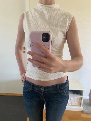 Vit ärmlös turtleneck linne med struktur - Snygg vit polotopp med hög hals och ärmlös design. Toppen är figurnära och har en stilren look. Skriv för frågor! Pris kan diskuteras. Storlek 34 passar också 36