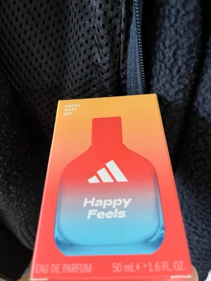 Adidas Happy Feels Eau de Parfum - Adidas Happy Feels Eau de Parfum i en snygg flaska med färgskiftning från rött till blått. Flaskan rymmer 50 ml och har en modern, sportig design med Adidas-loggan framtill. Perfekt för dig som gillar fräscha och energiska dofter.