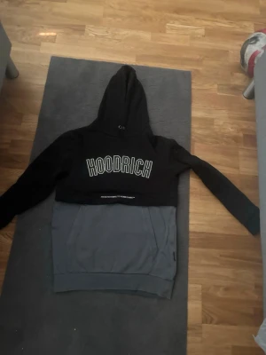 Svart och grå hoodie från Hoodrich - Snygg hoodie från Hoodrich i svart och grått med stor logga framtill. Tröjan har huva med dragsko och en stor magficka. Perfekt för dig som gillar streetwear och vill sticka ut med en cool look.