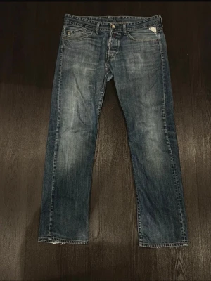 Jeans från Replay - Säljer ett par blå jeans från Replay med raka ben och slitna detaljer vid bensluten. Jeansen har klassisk femficksdesign, snygga slitningar och ljusare partier framtill. Perfekta för en avslappnad och trendig look. Storlek 33:32, hör av dig vid minsta fundering