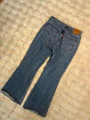 Levi's bootcut jeans - Ett par klassiska blå Levi's jeans med bootcut-modell och rå, fransad kant nertill. Jeansen har två bakfickor med den ikoniska Levi's-sömmen och läderpatch i midjan. Tillverkade i kraftig denim, perfekt för en avslappnad och trendig look.