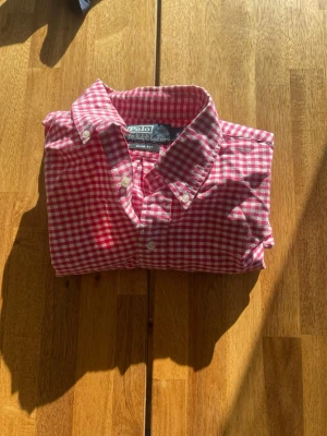 Rutig röd skjorta från Polo Ralph Lauren - Snygg röd- och vitrutig skjorta från Polo Ralph Lauren i slim fit-modell. Skjortan har klassisk krage, knappar framtill och korta ärmar. Perfekt för dig som gillar en preppy och stilren look.