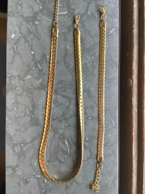Guldpläterat halsband i kedjemodell - Snyggt guldpläterat halsband i klassisk kedjemodell med platta, glänsande länkar. Halsbandet har en stilren och tidlös design som passar till många olika looks. Perfekt för dig som gillar accessoarer med lite extra bling. 43cm halsband. 18cm armband