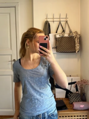 Blå topp från Trend Report - Säljer en ljusblå topp från Trend Report i storlek M. Toppen har korta ärmar, rund halsringning och ett diskret blommigt mönster i tyget. Materialet känns mjukt och har en lätt struktur som ger en snygg look till jeans eller kjol.