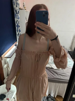 Beige/rosa offshoulder klänning från Nelly - Beige kortklänning med offshoulder och långa ärmar. Vetinte hur jag ska ha den riktigt. Armarna är svåra att förklara, sitter fast som i en tråd! Tillverkad i ett lätt och luftigt material, perfekt för sommaren. Skriv om du har frågor❣️