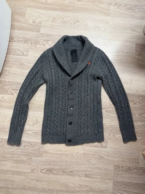 Grå kabelstickad kofta med sjalkrage - (Passar även S) Snygg grå kabelstickad kofta från G-star med sjalkrage och knäppning framtill. Koftan har långa ärmar, ribbade muddar och en liten orange detalj på axeln. Skriv för fler frågor💪🏼
