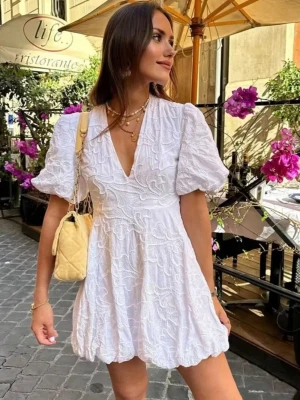 Vit kort klänning från Zara - Superfin vit kort klänning från Zara med puffärmar och v-ringning. Klänningen har broderade detaljer och en lätt volang nedtill. Perfekt för sommardagar och har en luftig passform.