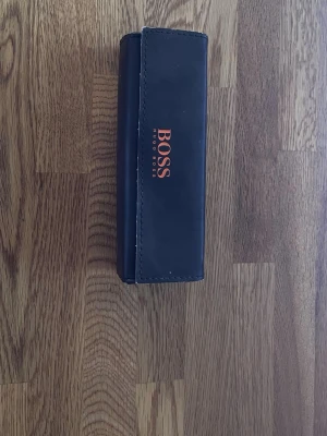 Hugo Boss fyrkantiga solglasögon - Snygga solglasögon från Hugo Boss med fyrkantig form och mörka linser. Bågarna har ett sköldpaddsmönster i bruna toner och kommer med ett svart fodral med BOSS-logga. Perfekt accessoar för en trendig look.
