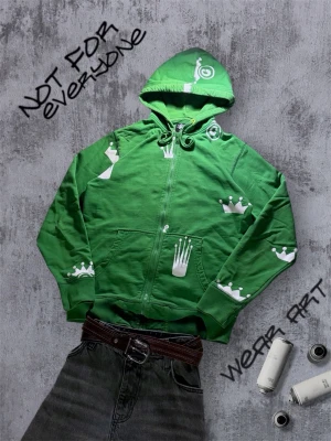 Vintage Stüssy Hoodie - Grön Stüssy hoodie med dragkedja och huva, dekorerad med vita kronmotiv och grafiska tryck. Hoodien har snörning i huvan och två fickor framtill. Perfekt för dig som gillar streetwear och unika plagg med konstnärlig touch. Storlek S. Skulle passa både till tjej och kille. 