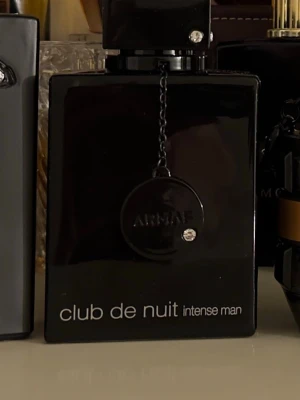 Armaf Club de Nuit Intense Man parfym - En stilren parfymflaska i svart glas från Armaf, Club de Nuit Intense Man. Flaskan har en fyrkantig form med en dekorativ kedja och rund medaljong framtill. Perfekt för dig som gillar eleganta och moderna dofter.