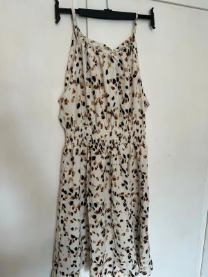 Mönstrad sommarklänning från Shein - Söt kortklänning från Shein med smala axelband och elastisk midja. Klänningen är vit med ett prickigt mönster i svart, brun och beige. Perfekt för varma dagar och har en luftig passform. Aldrig använd 🌸