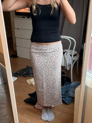 Blommig långkjol i beige  - Säljer en långkjol med blommigt mönster i beige och svart. Kjolen har en rak passform, liten slits bak och är tillverkad i ett mjukt, stretchigt material. Super söt och passar perfekt till sommaren 