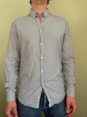 Randig skjorta med button down-krage - Snygg skjorta med smala blå och vita ränder, klassisk button down-krage och långa ärmar. Skjortan har vita knappar och är tillverkad i ett lätt bomullstyg. Perfekt för en stilren och avslappnad look.