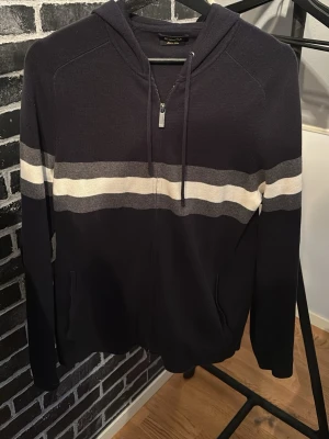 Mörkblå Massimo Dutti hoodie med ränder - Snygg mörkblå hoodie från Massimo Dutti med dragkedja och huva. Har två horisontella ränder i vitt och grått över bröstet och ryggen. Utrustad med fickor framtill och justerbar dragsko i huvan. Skriv vid frågor!🤗