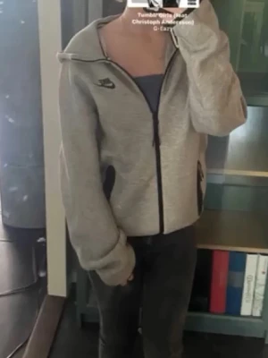 Grå zip hoodie från Nike - Snygg grå zip hoodie från Nike med svart dragkedja och svarta detaljer vid fickorna. Klassisk Nike-logga på bröstet. Tillverkad i mjukt material som känns skönt mot huden. Perfekt för dig som gillar sportig och avslappnad stil.
