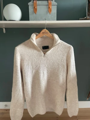 Beige halvzip-tröja från ASOS DESIGN - Säljer en beige stickad tröja från ASOS DESIGN med halvzip och hög krage. Tröjan är mjuk och har ribbade muddar vid ärmslut och nederkant. Perfekt för lager-på-lager och chill dagar. Endast testad