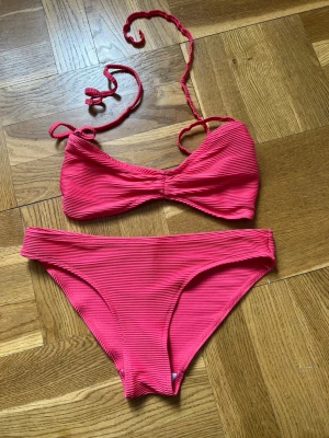 Rosa ribbad knytbikini Åhléns - Snygg rosa bikini från Åhléns med ribbad struktur och knyt i nacken. Överdelen har twistad front och justerbara axelband, underdelen är klassisk med medelhög midja. 