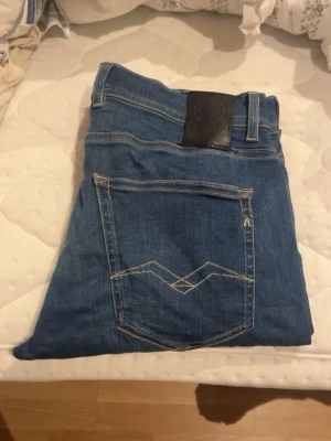 Blå jeans från Replay - Snygga blå jeans från Replay med klassisk femficksdesign och ljus tvätt. Jeansen har raka ben och detaljerade sömmar på bakfickan samt läderpatch med logga i midjan. Tillverkade i bomull med en skön passform.