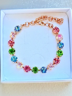 Armband med färgglada stenar - Armband i guldtonad metall med 8 mm stora, runda stenar. Stenarna är slipade och glittrar i blått, grönt, rosa. Justerbar kedja för perfekt passform. Perfekt accessoar för att addera färg till din stil. Näst sista bilden är en inspirationsbild som visar hur du kan kombinera med andra smycken tex Svedbom. Sista bilden är ett urval av färger som finns. 