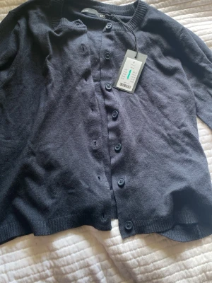 Lager 157 Mörkblå cardigan Stine S - Från lager 157 orginal pris 150kr.  Mörkblå cardigan från Stine med rund halsringning och knäppning framtill. Tröjan har långa ärmar och ribbade muddar vid ärmslut och nederkant. Perfekt att slänga över en t-shirt eller linne för en enkel och stilren look.