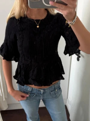 Volangblus med spetsdetaljer - Supersnygg svart blus med volanger och spetsdetaljer. Blusen har trekvartsärm med volangkant och en lös, flowy passform. Köpt för 300kr, säljer för 100kr.🌻