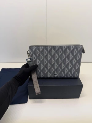 DlOR DIMOND MESSENGER POUCH - Säljer en fantastiskt fin Pouch i den ikoniska grå färgen med CD Diamond-mönstret. Väskan är en  klassiker och kombinerar lyx med praktisk funktion. Detaljer: Modell: CD Diamond Canvas & Smooth Calfskin. Färg: Grey (klassisk ljusgrå). Material: Slitstark belagd canvas med detaljer i mjukt kalvskinn Tillbehör: Kommer med originalbox, dustbag och den avtagbara axelremmen. Skickas spårbart och försäkrat.Tveka inte att höra av dig vid frågor eller om du vill ha fler bilder!