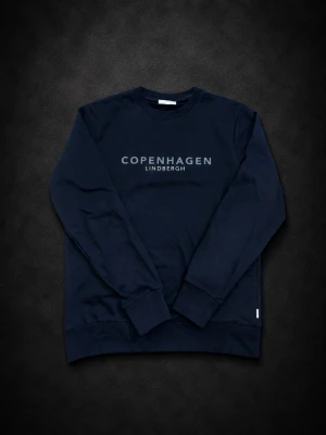 Svart sweatshirt från Lindbergh - Stilren svart sweatshirt från Lindbergh med trycket 'Copenhagen' på bröstet. Tröjan har rund halsringning, långa ärmar och ribbade muddar. Perfekt för en avslappnad och trendig look.