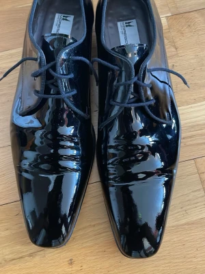 Svarta lackloafers från Moreschi - Säljer ett par svarta loafers från Moreschi i glansigt lackläder. Skorna har en elegant, fyrkantig tå och klassisk snörning. Tillverkade i Italien och har en stilren design som sticker ut. Perfekta för dig som vill ha en dressad look.