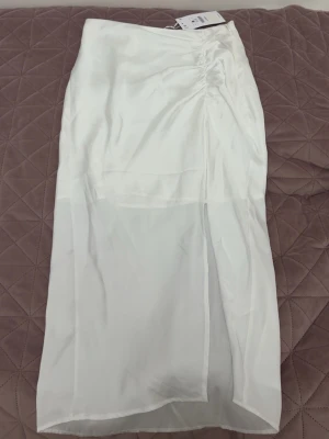 Vit satinkjol med slits - En vit medellång kjol i satin med slits framtill. Helt oanvänd