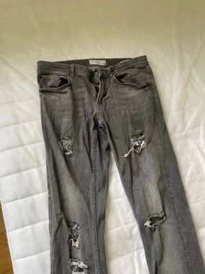 Grå slitna jeans från REBEL - Snygga grå jeans från REBEL i slim/regular fit med slitna detaljer för en trendig look. Perfekta till både vardag och streetwear.  * Märke: REBEL * Modell: Slitna jeans * Storlek: W30 / L32 * Färg: Grå (washed) * Passform: Slim/regular * Skick: Bra använt skick – slitningarna är designade och en del av stilen * Material: Jeans/denim  Bekväma och stilrena, passar till allt från hoodie till skjorta. Säljes då de inte används längre.  📦 Kan skickas snabbt 💬 Hör av dig vid frågor! Skicka bud!!!