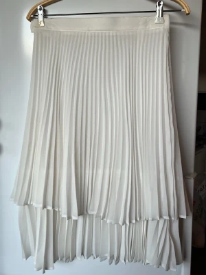 Vit kjol med volang   - Vit plisserad kortkjol i fint svalt material som är perfekt till sommar som avslutningar, student eller annat. Kjolen har en mjuk, flowy känsla och stängs med dragkedja i sidan. Perfekt för sommarens aktiviteter 🌟