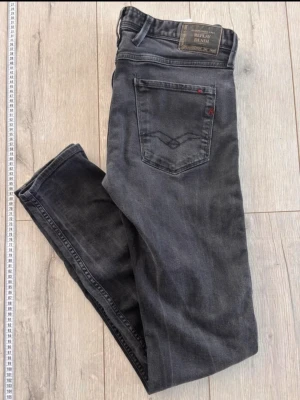 Svarta replay anbass - Snygga svarta slim fit jeans från replay med klassisk femficksdesign och diskret broderad detalj på bakfickan. Jeansen har en tvättad look och smal passform som sitter tajt längs benen. Perfekta för en trendig och avslappnad stil. Replay anbass helt oanvända i storlek w32 l36