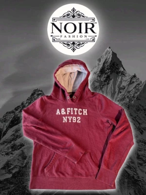 Vinröd hoodie från Abercrombie&Fitch - Snygg vinröd hoodie från A&Fitch med vit text 'A&FITCH NY92' på bröstet. Hoodien har en stor luva med ljus insida, dragsko och känguruficka framtill. Perfekt för kalla dagar och riktigt skön att mysa i.