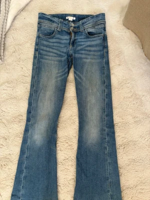 Blå bootcut jeans från Gina Tricot - ⚠️Fläckarna på baksidan är endast smuts som går att få bort i tvätt ⚠️ Snygga blå bootcut jeans från Gina Tricot med dubbla knappar och klassisk femficksdesign. Jeansen har en lätt tvättad look och markerade sömmar. Perfekta för dig som gillar en avslappnad men trendig stil. Jag tvättar dom innan dom skickas