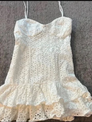 Klänning Zara  - Söt vit klänning med tunna axelband och volangkant nertill. Klänningen har ett broderat spetsmönster över hela plagget och en figurnära passform upptill. Perfekt för sommarens alla tillfällen.
