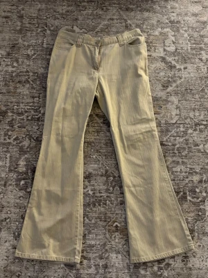 Beige utsvängda byxor - Snygga beige byxor med utsvängda ben och coola fickor med lock och knapp bak. Klassisk femficksmodell framtill och breda hällor för bälte. Perfekta för dig som gillar retrovibbar och vill sticka ut lite extra. 42 cm i midjan tvärs över och 76 cm innerben✨