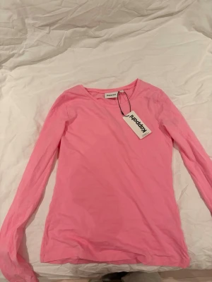 Rosa långärmad topp från Kappahl - En enkel och snygg rosa långärmad topp från Kappahl i mjuk bomull. Modellen har rund halsringning och en klassisk passform som funkar till allt. Perfekt att styla med jeans eller kjol för en fräsch look.