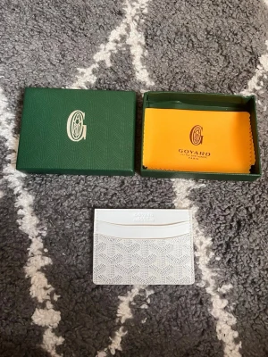 G-plånbok - Snygg och stilren i färgen vit med deras ikoniska mönster. Plånboken har flera kortfack och är tillverkad i skinn med tryckt logga framtill. Perfekt för dig som vill ha något exklusivt och smidigt i fickan.  