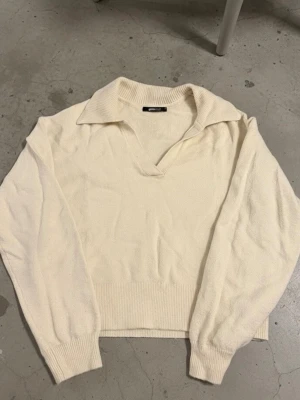 Krämvit stickad tröja med krage - Snygg krämvit stickad tröja från Gina Tricot med bred krage och v-ringning. Tröjan har långa ärmar och ribbade muddar vid ärmslut och nederkant. Perfekt för en stilren och avslappnad look.