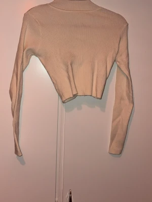 Beige ribbad cropped omlottopp - Trendig vit  cropped omlottopp i ribbat material. Långärmad modell med snygg omlottdesign framtill som ger en cool och modern look. Perfekt att styla med höga jeans eller kjol för en avslappnad men chic outfit.