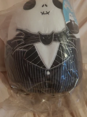 Squishmallow Jack Skellington - Mjuk och gosig Squishmallow i form av Jack Skellington från The Nightmare Before Christmas. Vit och svart med broderade detaljer och randig kostym. Perfekt som prydnad eller kramkompis för alla som gillar Disney och Halloween.