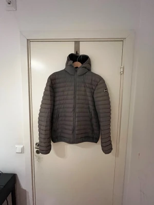 Colmar jacka - Snygg grå dunjacka från Colmar med quiltad design och fast huva. Jackan har dragkedja framtill, två sidofickor och en diskret logga på ärmen. Perfekt för kalla vinterdagar och riktigt lätt att bära. Storlek 48, skulle säga att den passar S. Mycket bra skick utan några defekter. 