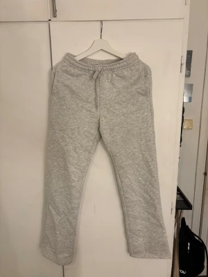 Grå mjukisbyxor med dragsko - Säljer ett par klassiska grå mjukisbyxor med resår i midjan och justerbar dragsko. Byxorna har raka ben och två sidofickor. Perfekta för chill dagar hemma eller när du vill vara bekväm. Materialet känns mjukt och skönt mot huden.