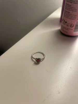 Pandora promisering  - Snygg silverfärgad ring med en röd hjärtformad sten i mitten. Den är i silver och från de trendiga märket Pandora. Ringen har små pärldetaljer runt stenen som ger en extra touch. Perfekt accessoar för att lyfta din stil. Storlek ser du på de sista bilderna. 