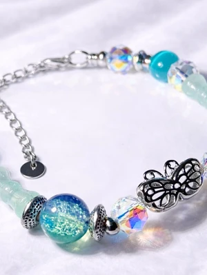 Armband med glaspärlor och fjäril - Snyggt armband med skimrande pärlor i blått, turkost och transparent samt en silverfärgad fjärilsdetalj. Armbandet har justerbar kedja och mix av metall och glas. Perfekt accessoar för dig som gillar unika detaljer och färg.